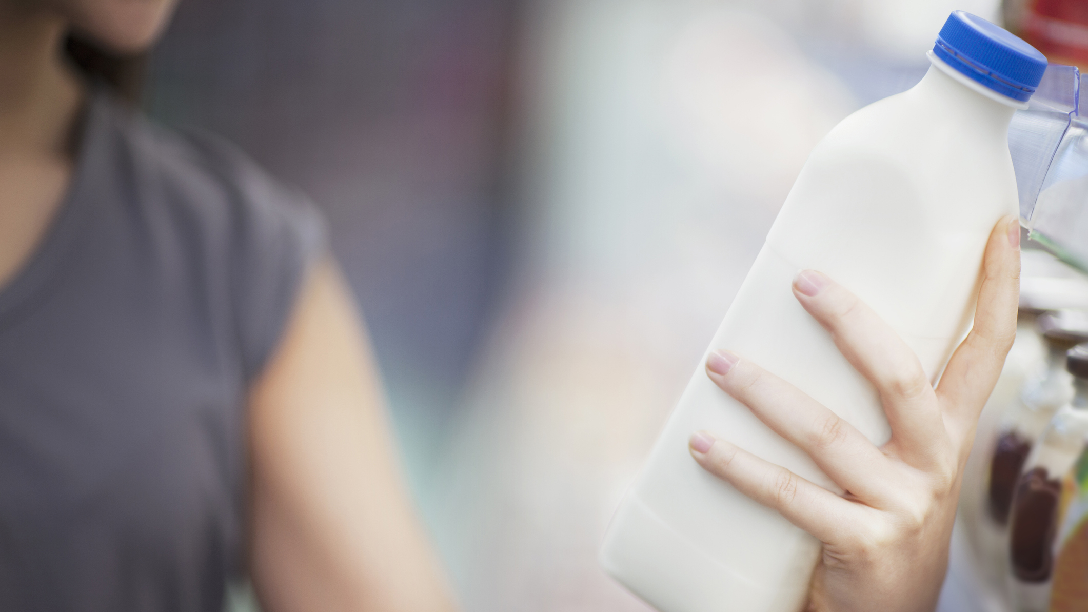 Woman checking label on milk in grocery store dairy section.